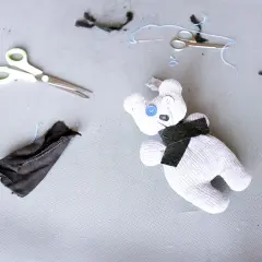 Uroczy kot ze skarpetki, z guzikami zamiast oczu, leży obok nożyczek i resztek materiału.