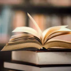 Otwarta książka na stosie innych. Idealne miejsce, gdzie oddać książki za darmo, to biblioteka lub punkt wymiany.