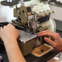 Ręce prowadzą czarny materiał przez maszynę, tworząc precyzyjny szew kryty na maszynie.
