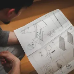 Mężczyzna czyta instrukcję montażu mebli z rysunkami technicznymi.