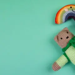 Miś ze skarpetki w zielonym sweterku leży obok tęczy.