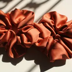 Dwa satynowe scrunchie w kolorze miedzianym, idealne do nauki, jak uszyć scrunchie.