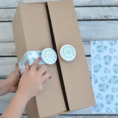 Ręce ozdabiają kartonową szafkę zieloną taśmą z liśćmi i okrągłymi uchwytami.