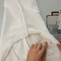 Ręce dopasowują białe spodnie do maszyny do szycia, pokazując, jak zwęzić spodnie w kroku.