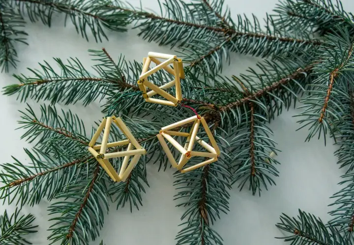 Trzy ozdoby choinkowe ze słomy w kształcie brył geometrycznych wiszą na gałęzi świerku.