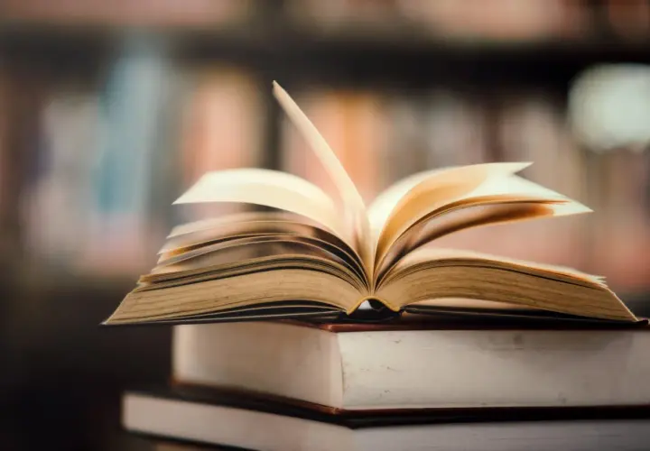 Otwarta książka na stosie innych. Idealne miejsce, gdzie oddać książki za darmo, to biblioteka lub punkt wymiany.