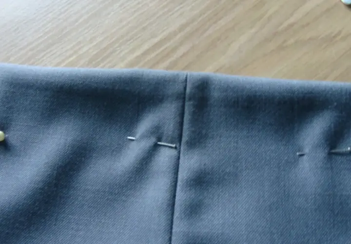 Szare spodnie z zaznaczonymi zaszewkami, gotowe do szycia. Szpilki trzymają materiał.