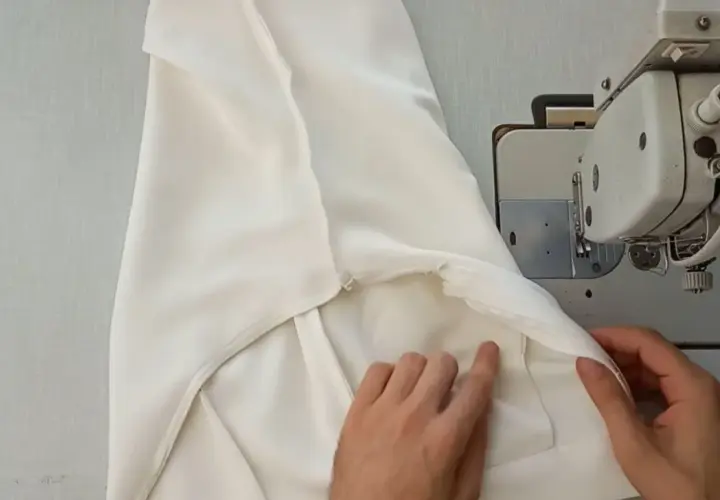 Ręce dopasowują białe spodnie do maszyny do szycia, pokazując, jak zwęzić spodnie w kroku.