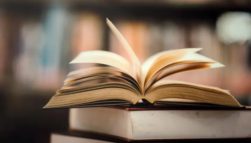 Otwarta książka na stosie innych. Idealne miejsce, gdzie oddać książki za darmo, to biblioteka lub punkt wymiany.