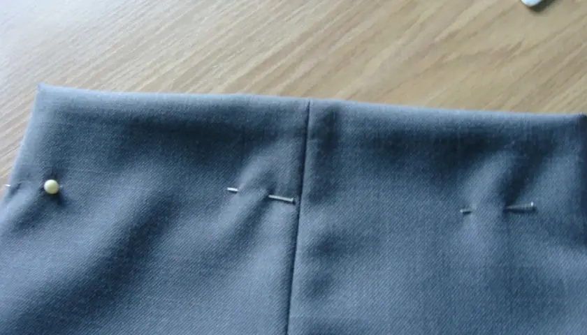 Szare spodnie z zaznaczonymi zaszewkami, gotowe do szycia. Szpilki trzymają materiał.
