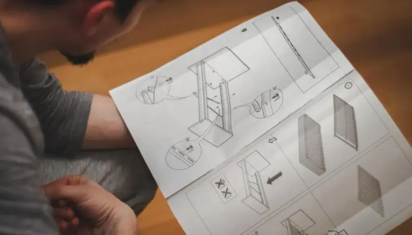 Mężczyzna czyta instrukcję montażu mebli z rysunkami technicznymi.