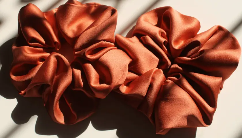 Dwa satynowe scrunchie w kolorze miedzianym, idealne do nauki, jak uszyć scrunchie.