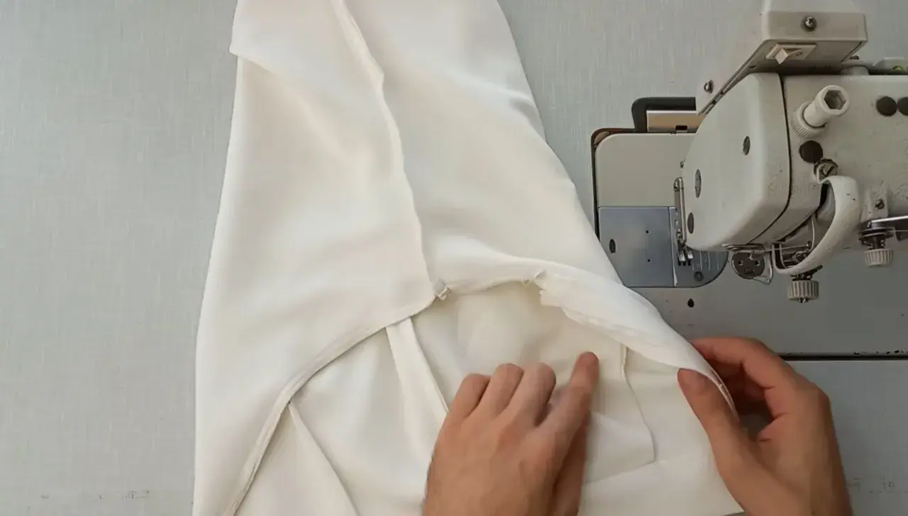 Ręce dopasowują białe spodnie do maszyny do szycia, pokazując, jak zwęzić spodnie w kroku.