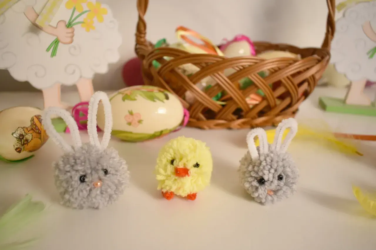 Wielkanocne ozdoby: pompony zajączki i kurczaczek, koszyk z pisankami.